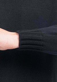 Maglione nero lavorato a maglia con polsini a costine. Il materiale presenta un motivo testurizzato. Ha una manica aderente per un aspetto allungato.