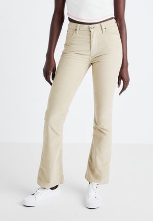 Beige corduroy flare broek met een hoge taille, voorzakken en een knoopsluiting. Draagt met witte sneakers en een cropped top.