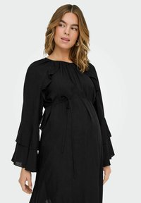 Vestido de maternidad negro con escote redondo, largas mangas con volantes, cintura con lazo y textura plisada. Diseño simple y fluido.