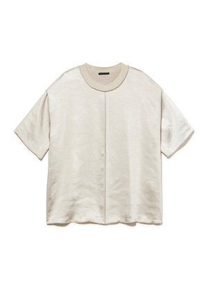 T-shirt surdimensionné beige clair en tissu doux. Présente un col rond, des manches courtes et un détail de couture centrale. Texture lisse avec un léger éclat.