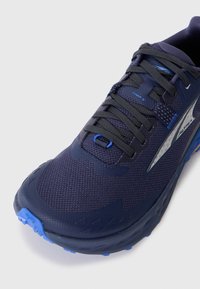 Chaussure de sport bleu foncé avec lacets noirs, tige en mesh respirant et semelle en caoutchouc bleu clair. Logo de la marque sur le côté et texte "Timp 5" près des lacets.