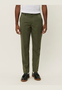 Pantalons ajustés vert olive avec une coupe droite, présentant une texture lisse, des passants de ceinture et des poches latérales. Portés avec des chaussures noires.