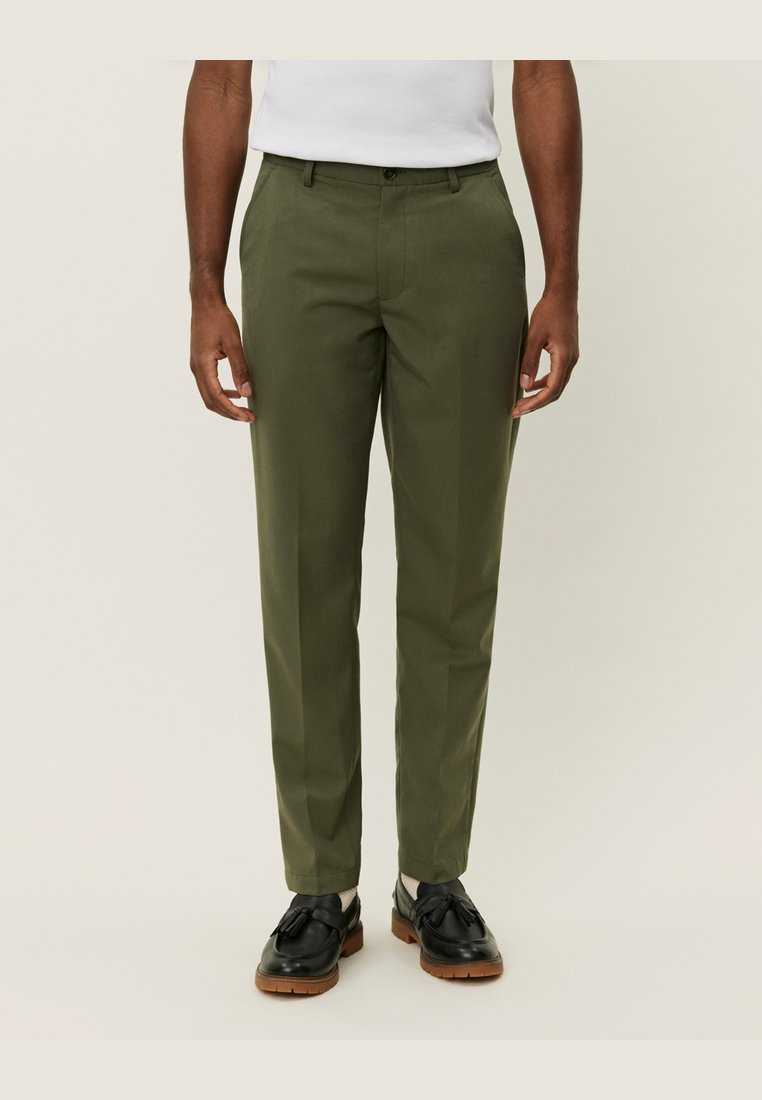 Pantalons ajustés vert olive avec une coupe droite, présentant une texture lisse, des passants de ceinture et des poches latérales. Portés avec des chaussures noires.