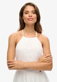 Witte haltertop jurk met geborduurde patronen, gegolfde halslijn en dunne bandjes. De stof is lichtgewicht met een zachte textuur.