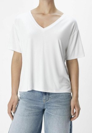 Person iført en løs hvid V-hals kortærmet skjorte, stoppet ned i lyseblå højtaljede jeans, synlig fra nakke til hofter.