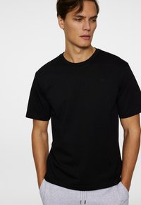 T-shirt noir à manches courtes avec un col rond, fabriqué en matériau doux, présentant un logo en relief subtil sur la poitrine.