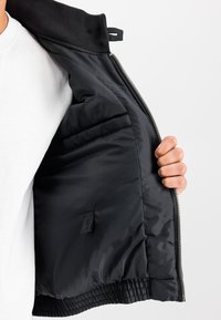 Must bomberjakk sileda, läikiva voodri ja soonikkoelise kraega, sisemine tasku ja esiküljel lukuga sulgur.