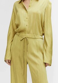 Chemise verte à manches longues avec un devant boutonné et un pantalon ceinturé assorti, en tissu texturé à rayures.