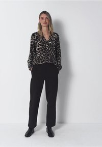 Bluzka w panterkę z długimi rękawami, dekoltem w serek i miękką teksturą, zestawiona z czarnymi spodniami z wysokim stanem i czarnymi botkami za kostkę.