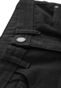 Pantalons en denim noir avec fermeture à bouton en métal et coutures contrastées. Gros plan de la taille avec passants de ceinture et tissu texturé.