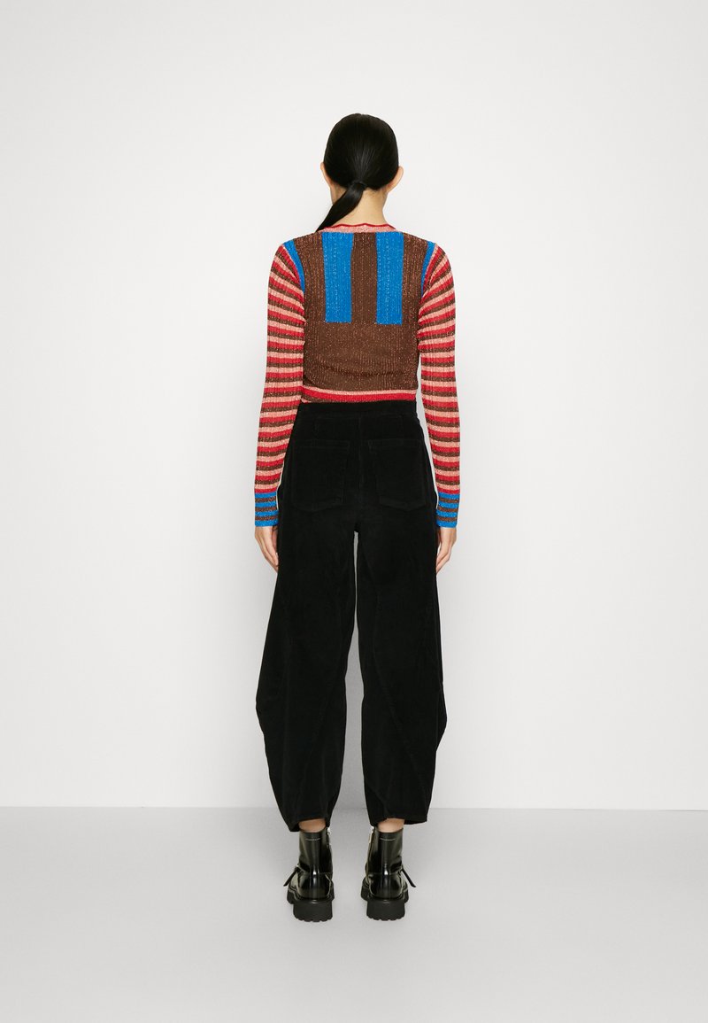 Haut à manches longues rayé avec des nuances de marron, bleu et rouge ; pantalon noir à jambes larges ; matériaux texturés ; bottines noires à semelles épaisses.