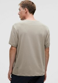 Világos bézs, rövid ujjú póló, puha anyagból, kerek nyakkal. Laza szabású, és egy kis logó található a hátsó alsó részen.