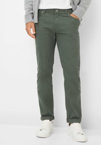 Olijfgroene chino's met een rechte pasvorm, voorzien van een knoop- en ritssluiting, zijzakken en opgerolde manchetten, gedragen met witte sneakers.