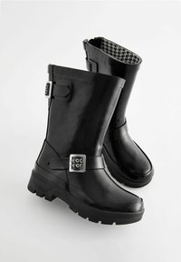 Bottes de pluie en caoutchouc noir avec une finition brillante, dotées d'une sangle à boucle et d'un motif pied-de-poule à l'intérieur. Semelle crantée pour une meilleure adhérence.