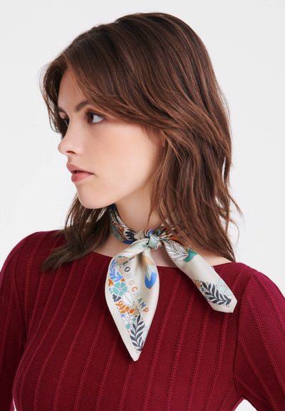 Silk scarf featuring a floral pattern in blue, green, orange, and beige, tied around the neck with a bow. The background is neutral.