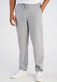 Grijze joggingbroek met een elastische tailleband en verstelbaar trekkoord. Gemaakt van zachte stof; zijkanten zakken; taps toelopend beenontwerp. Gedragen met witte sneakers.