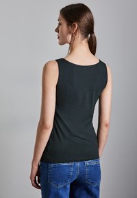 Top nero senza maniche, scollatura rotonda, realizzato in tessuto morbido. Abbinato a jeans in denim blu con tasche posteriori e leggermente sbiaditi.