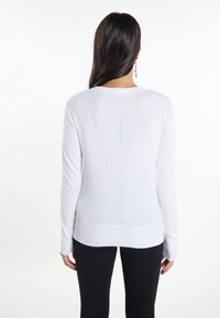 Maglione lavorato a maglia bianco a maniche lunghe con scollatura tonda, caratterizzato da una cucitura posteriore sottile e orlo a coste, abbinato a pantaloni neri.