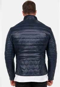 Navy blauwe leren gewatteerde jas met een hexagonaal textuurpaneel op de onderrug, staande kraag en ritssluiting bij de manchetten.