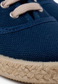 Marineblauwe canvas schoen met een gestructureerde bovenkant, beige veters en een natuurlijke jute touwzool. Close-up weergave die de materiaaldetails benadrukt.