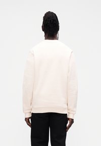 Ροζ ανοιχτή φούτερ με στρογγυλή λαιμόκοψη και μακρι�ά μανίκια, με ριμπ μανσέτες και τελείωμα, συνδυασμένο με μαύρο παντελόνι.