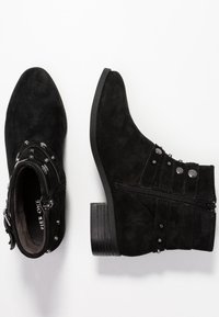 Botas de ante negras hasta el tobillo con puntera redondeada, cremallera lateral, tachuelas decorativas y un tacón apilado. Superficie texturizada y diseño minimalista.