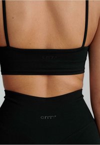 Zwarte sportbh met dunne bandjes, gladde textuur en subtiel logo-detail; gecombineerd met hoge zwarte leggings met een vergelijkbare textuur.