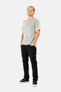 Camiseta de algodón verde claro con un acabado texturizado, combinada con jeans negros de pierna recta y zapatillas negras de corte bajo con suelas blancas.