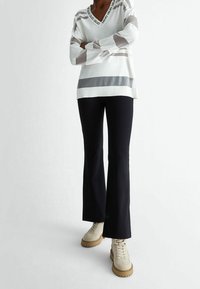 Pullover bianco a collo a V con righe orizzontali grigie, abbinato a pantaloni neri a zampa d'elefante e stivaletti beige con lacci.