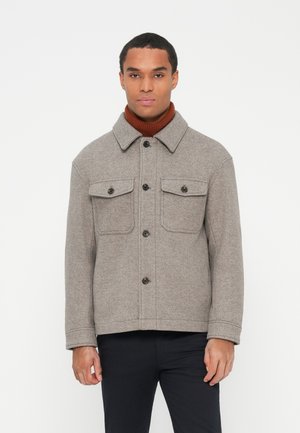 Gray wool jacket with a collar, featuring two chest pockets, black buttons, and a textured finish, worn over a brown turtleneck.