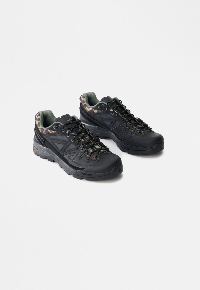 Ζευγάρι μαύρα και καμουφλάζ ορειβατικά παπούτσια με χοντρές σόλες και σχέδιο με κορδόνια σε λευκό φόντο.