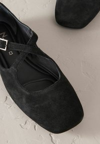 Zwarte suède schoenen met een kruisband en vierkante neus. Gestructureerd oppervlak en gevoerde binnenkant, met een zilveren gespaccent.