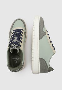 Zapatillas verdes claras y grises con un collar acolchado, acentos texturizados, cordones azul marino y una suela de goma blanca. Etiqueta de talla 42 visible en el interior.