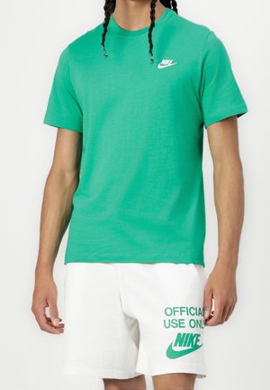 Personne portant un t-shirt Nike vert et un short blanc avec le texte vert « Usage officiel uniquement » et le logo Nike sur la jambe gauche.