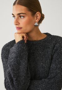 Mørkegrå tekstureret sweater med løs pasform og brede manchetter. Modellen bærer geometriske sølvøreringe med vandrette striber.