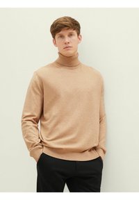 Pull col roulé beige clair en tricot doux, doté de manches longues et d'un col côtelé, associé à un pantalon noir ajusté.