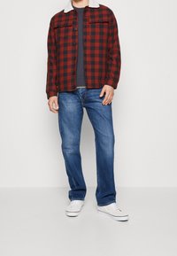 Punamusta ruudullinen kauluspaita, jossa on valkoinen keinovaariakaulus, napit edessä, päällä harmaa neule ja siniset farkut. Valkoiset lenkkarit.