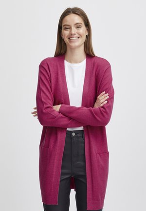 Cárdigan fucsia con mangas largas y diseño de frente abierto. Presenta dos bolsillos frontales y una textura suave, combinado con una camiseta blanca y pantalones oscuros.