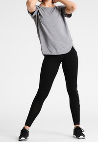 Grå t-shirt med kort ärm och rundad nederkant, kombinerad med svarta leggings med vit textdetalj. Sportskor fulländar outfiten.