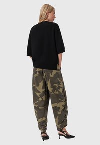Maglione nero oversize a maniche corte abbinato a pantaloni cargo larghi con motivo camouflage in tonalità verdi, accentuati da orli affusolati e tasche.