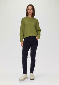 Overmatige groene trui met een horizontale ribbelstructuur, gecombineerd met donkerblauwe corduroypantalons en crèmekleurige enkellaarsjes.