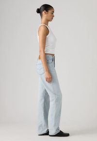 Φωτεινό μπλε τζιν με ίσια γραμμή στο πόδι, σχέδιο με πέντε τσέπες και ταμπελάκι από δέρμα ταμπά στο πίσω μέρος. Φοράται με λευκό αμάνικο κορμάκι.