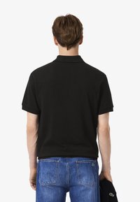 Polo nero con maniche corte e colletto classico, realizzato in un tessuto morbido. Dettagli notevoli includono un piccolo logo sul retro.
