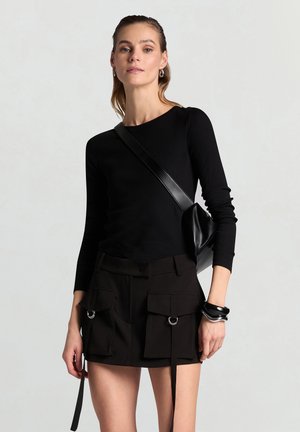 Top nero a maniche lunghe a coste abbinato a una minigonna nero a vita alta con due tasche frontali e anelli laterali, con una piccola borsa a tracolla.