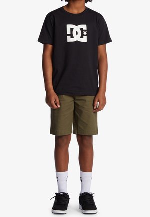 Czarny bawełniany t-shirt z białym logo, oliwkowo-zielone szorty, białe skarpetki za kostkę i czarne trampki. Skupienie na stylu casual streetwear.