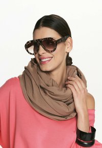 Brązowe, oversize'owe okulary przeciwsłoneczne z wzorzystą oprawką, zestawione z beżowym szalem i luźną, różową bluzką z odkrytymi ramionami.