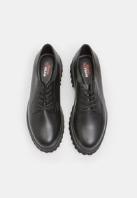 Chaussures en cuir noir avec une texture lisse, bout rond, design à lacets et semelle en caoutchouc épaisse. Présente un marquage "Red FOAM" sur la semelle intérieure.