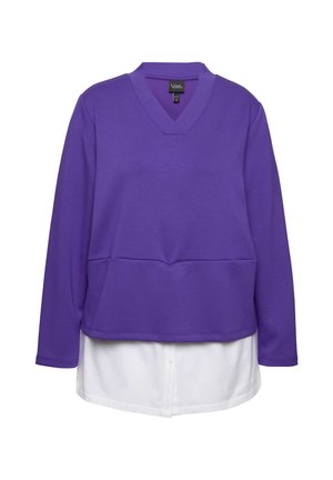 Sweter z dekoltem w serek, z długim rękawem, w kolorze fioletowym, nałożony na białą koszulę z guzikami. Miękka faktura, swobodny fason, z rozcięciem u dołu.