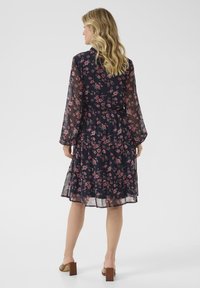 Navy floral dress with long sheer sleeves, a fitted waist, and tiered skirt. Features a floral pattern in pink and white on a dark background.