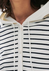 Felpa con cappuccio a righe in bianco e blu navy, con chiusura a bottoni, cordino e una texture morbida.